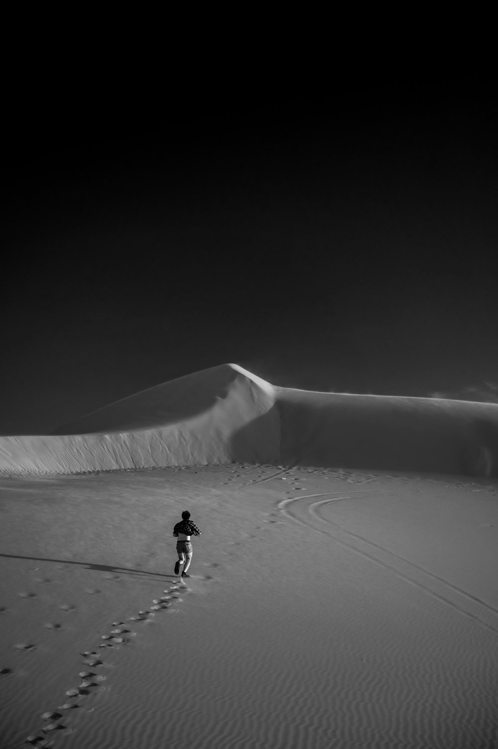 a man walking across a sandy desert under a dark sky