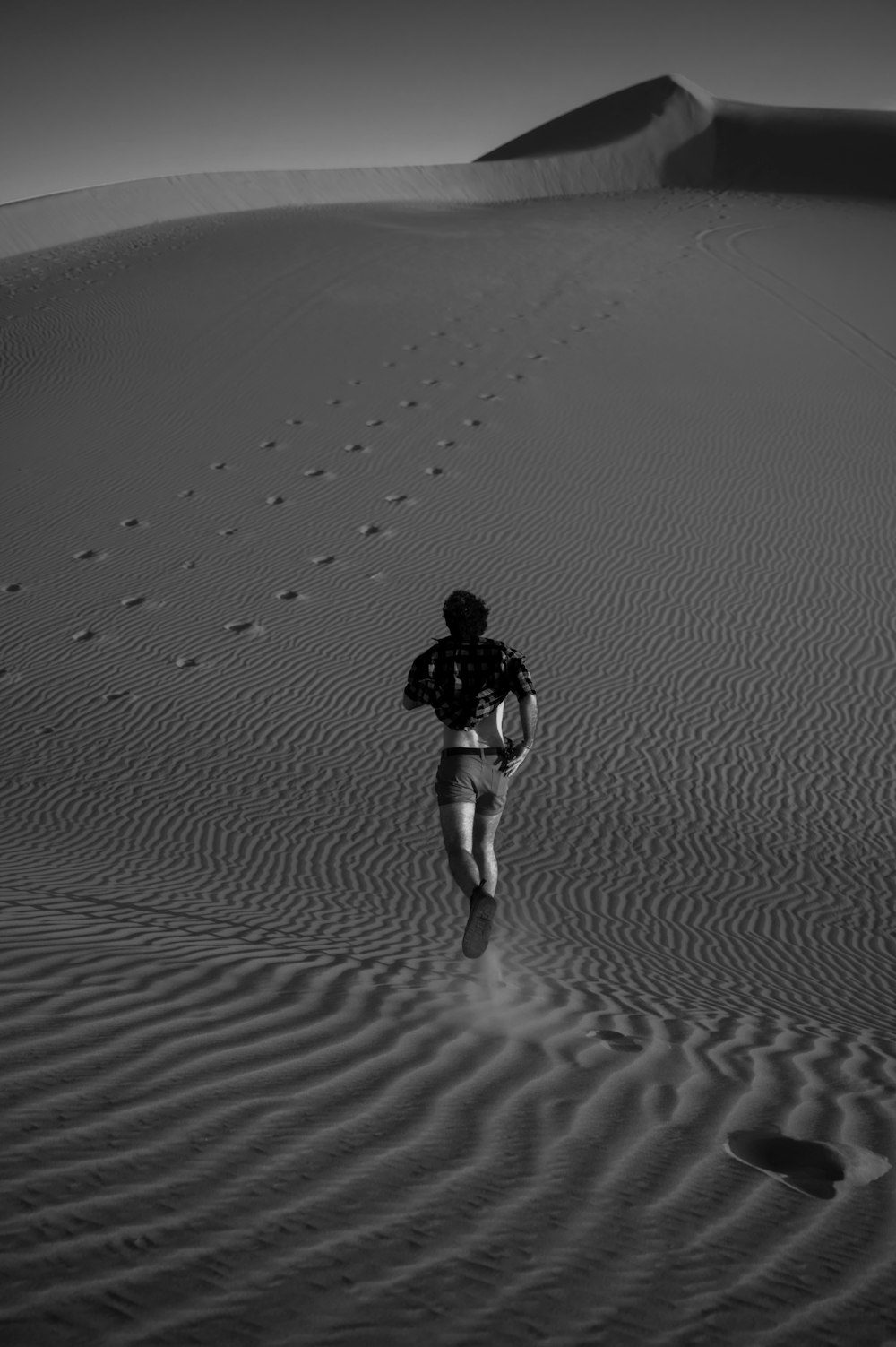 a man walking across a sandy field with footprints in the sand