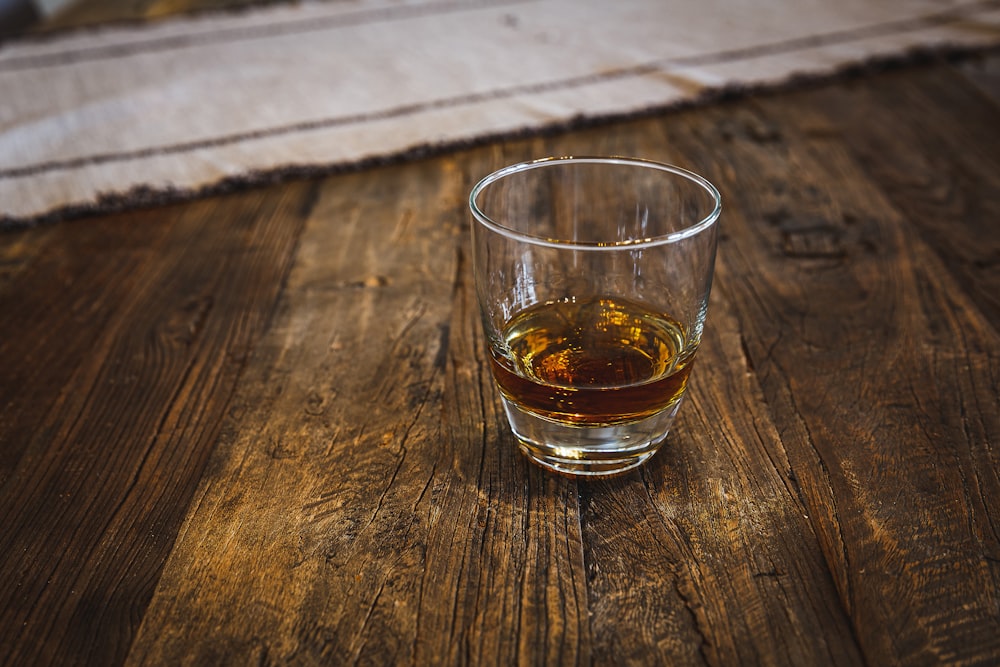 a glass of whiskey sitting on a wooden table