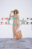 a woman in a bikini and hat holding a bag