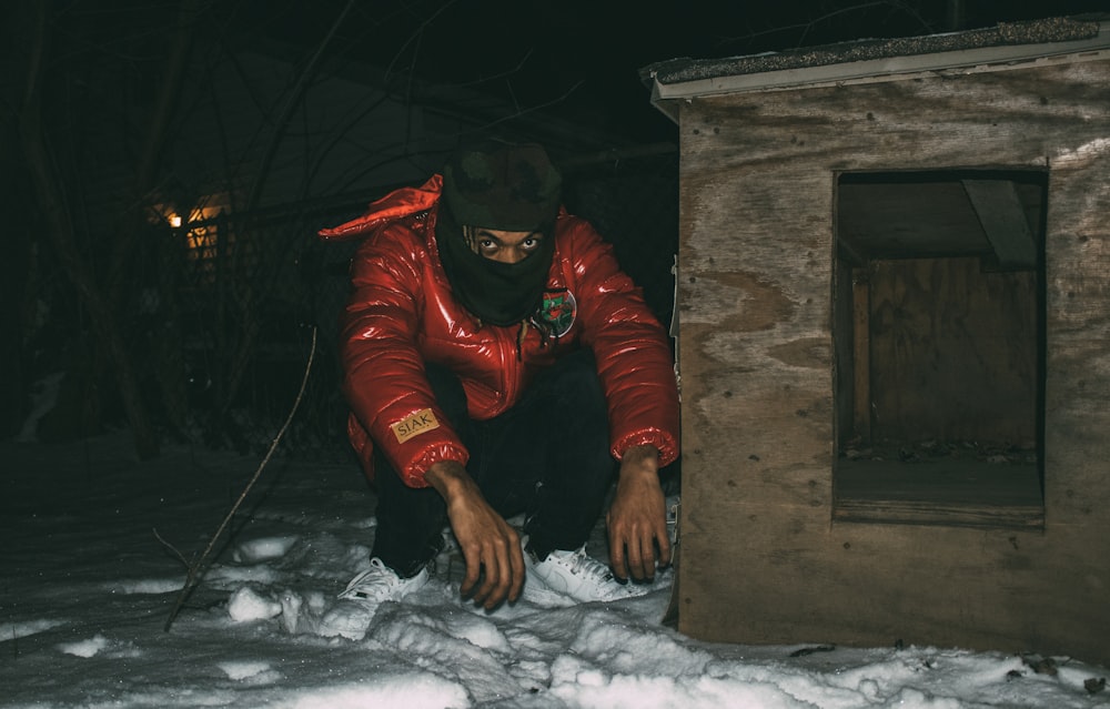 a man in a red jacket leaning against a building in the snow