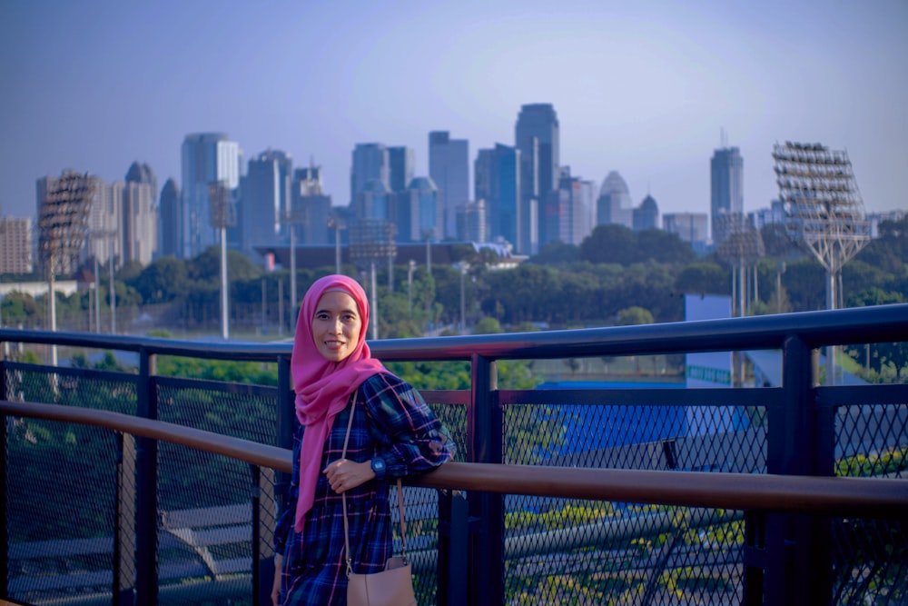 a woman standing on a bridge with a city in the background