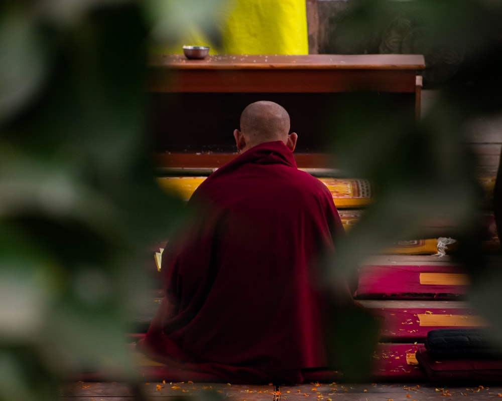 a monk in a red robe sitting on a bench