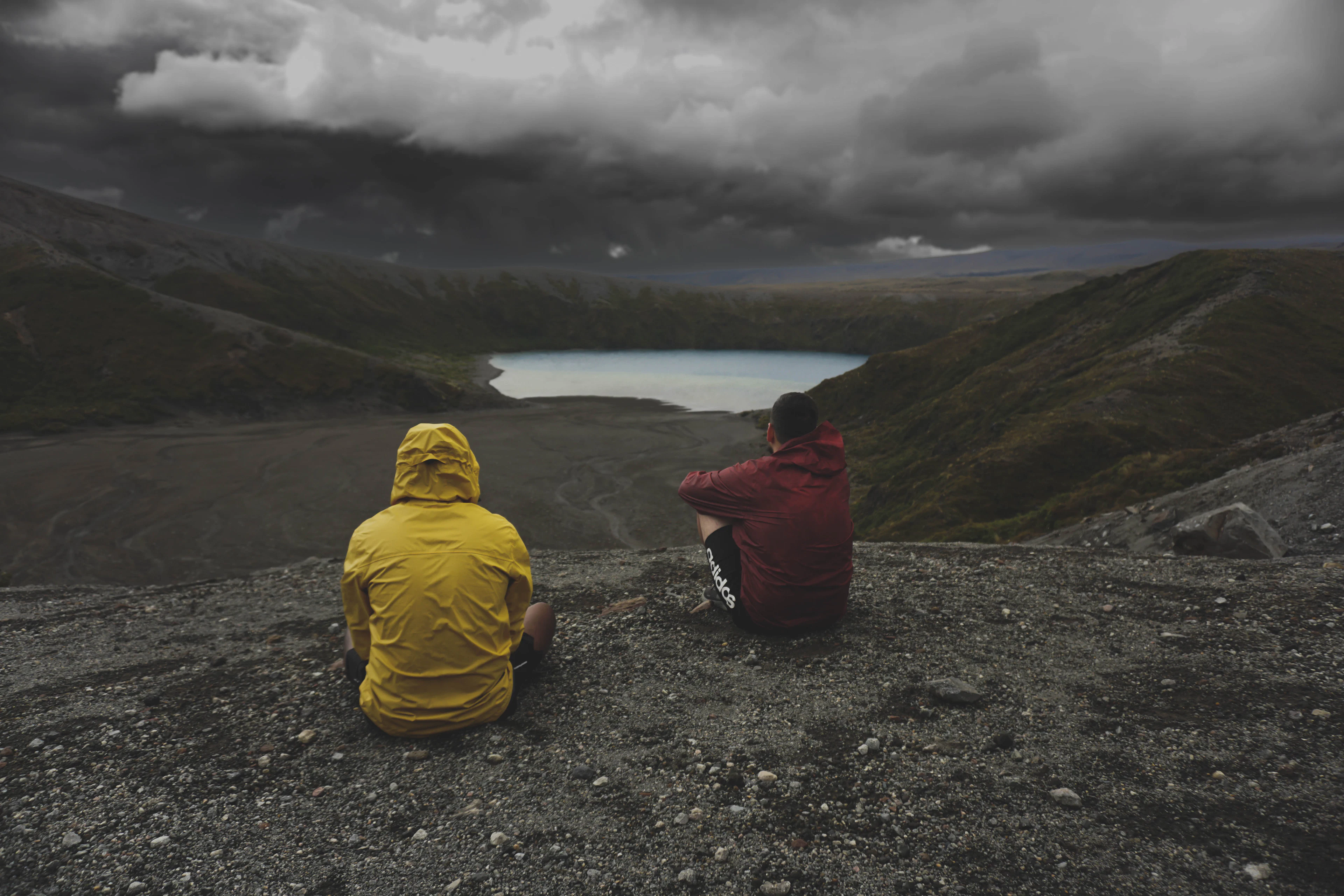 Two walkers sitting on a volcanic slope above Lower Tama Lake in Tongariro National Park