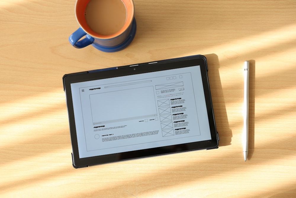 a tablet computer sitting on top of a wooden table next to a cup of coffee