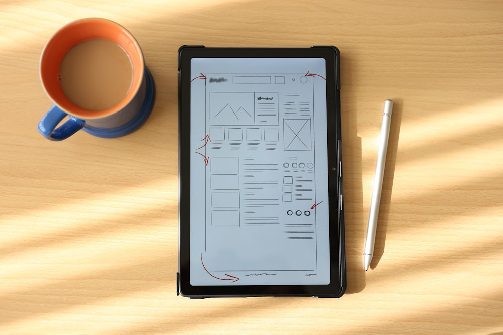 a tablet computer sitting on top of a wooden table next to a cup of coffee