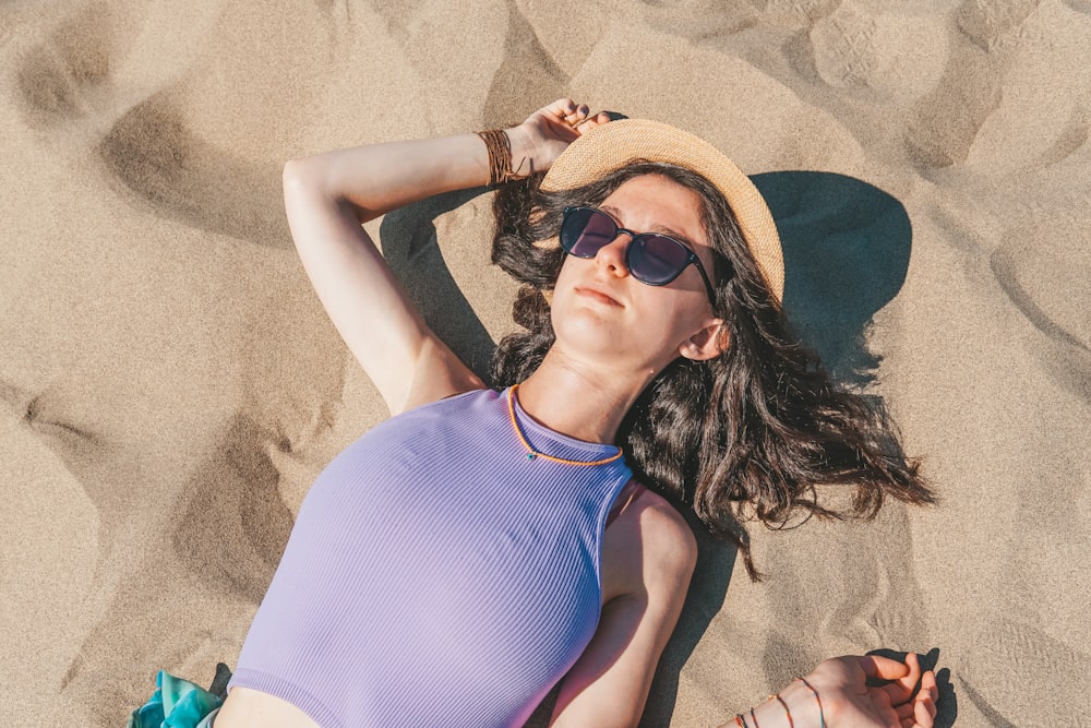 a woman laying in the sand wearing a hat and sunglasses