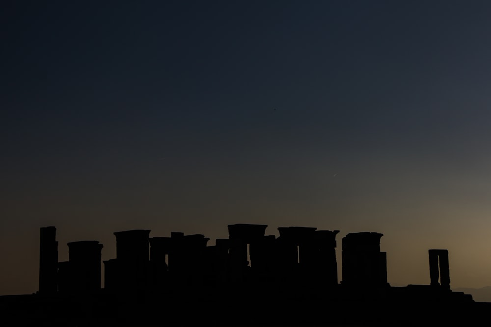 the sun is setting behind the silhouette of a group of stonehenges