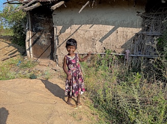 A young girl proudly holding her school books with a big smile in front of a modest home.