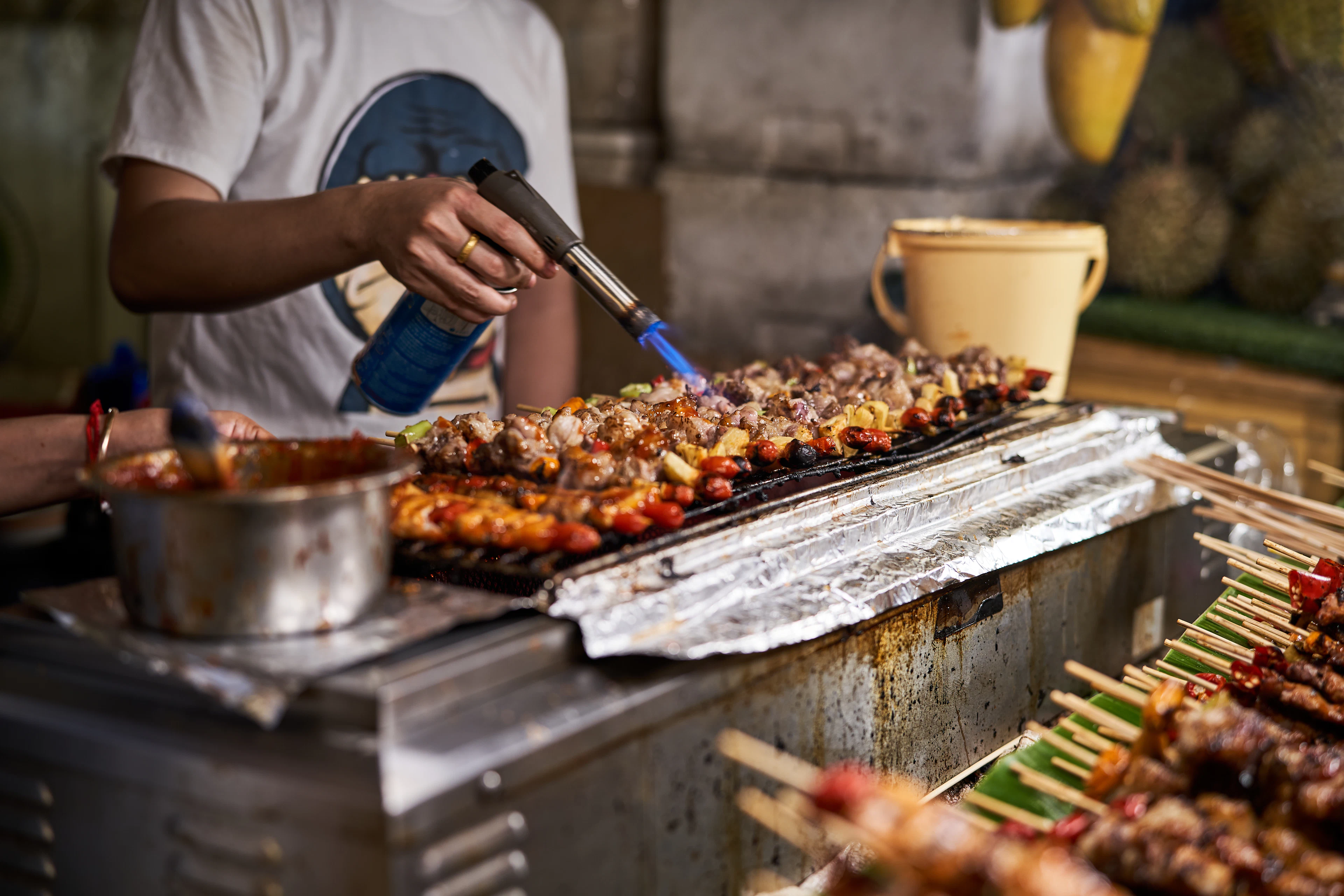 A street cook grilling skewers at a night market in Bangkok