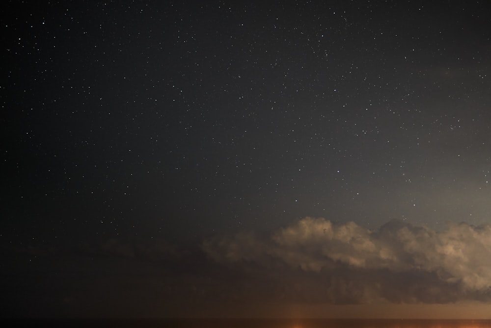a night sky with stars and clouds over the ocean