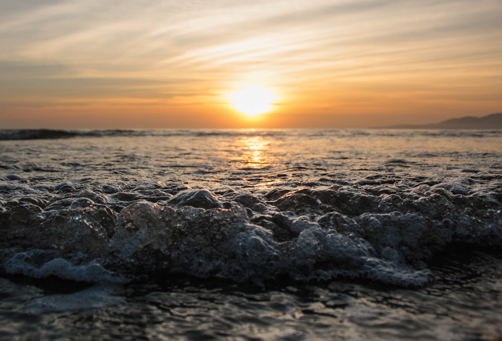 the sun is setting over the ocean with waves