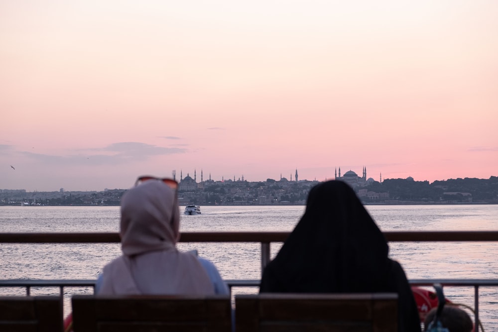 two women sitting on a bench looking out at the water