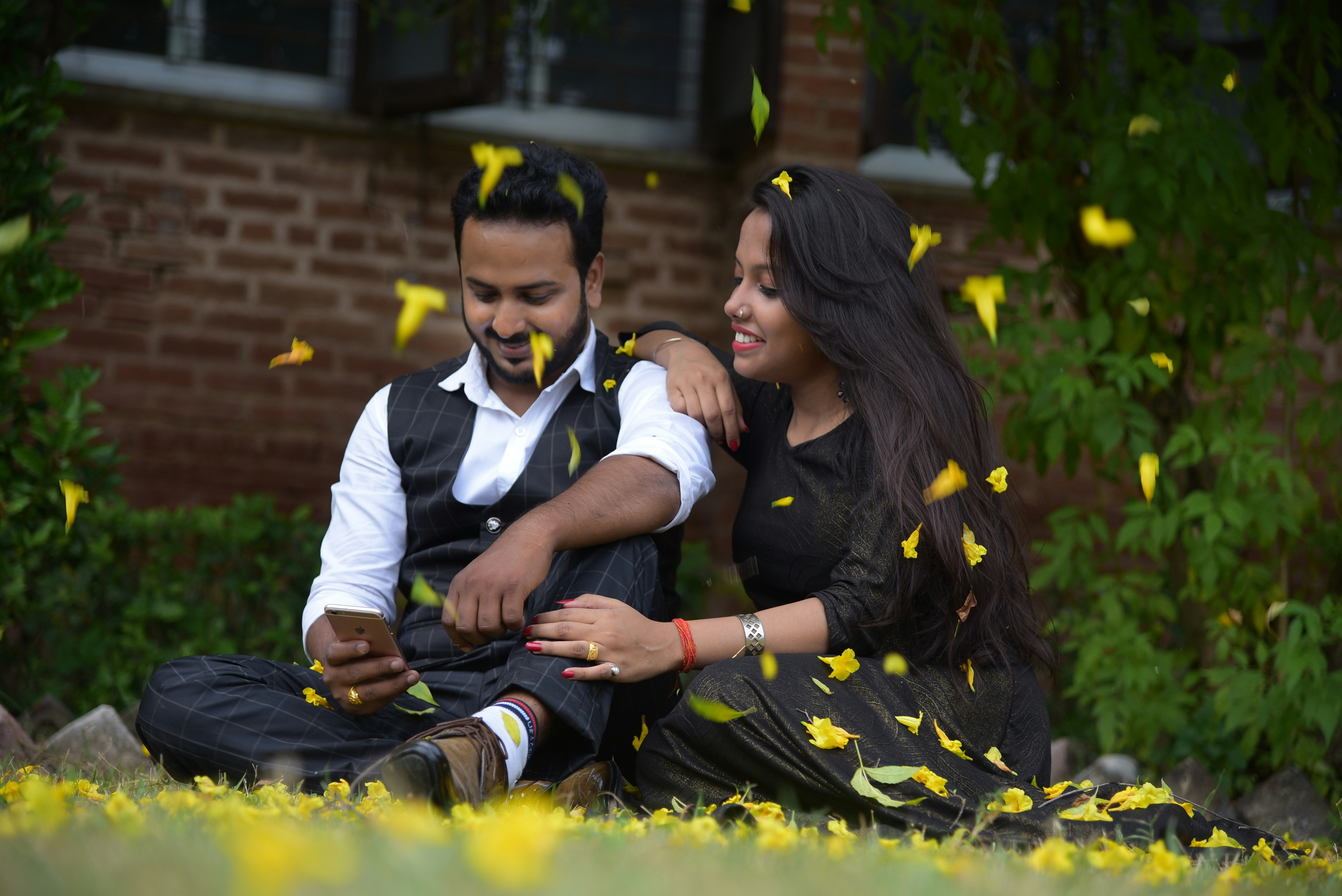 Un hombre y una mujer sentados en el suelo mirando un teléfono celular. ¿Qué es lo más difícil de una relación a distancia?