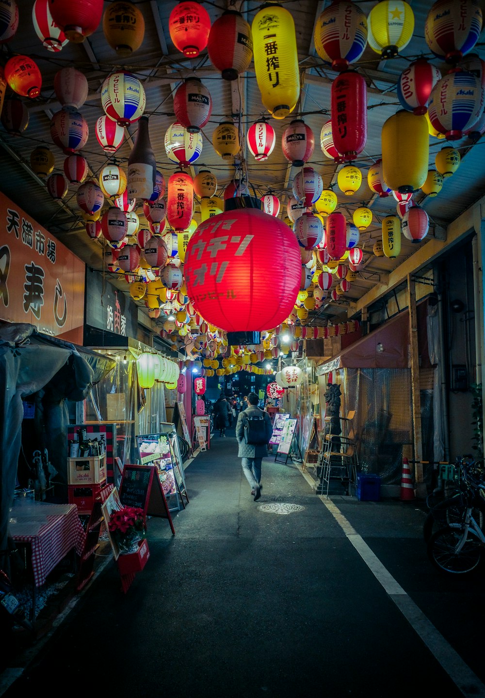 a person walking down a street with lots of lanterns hanging from the ceiling