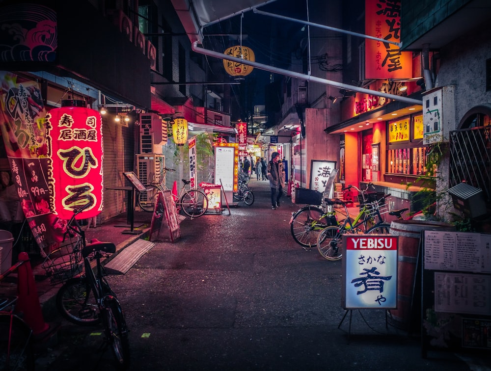 a narrow alley way with neon signs and bicycles
