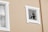 A beige wall with two windows, one of which is intact and the other has a shattered glass pane. The frames around the windows are white, and the shattered window reveals cracks and missing pieces.