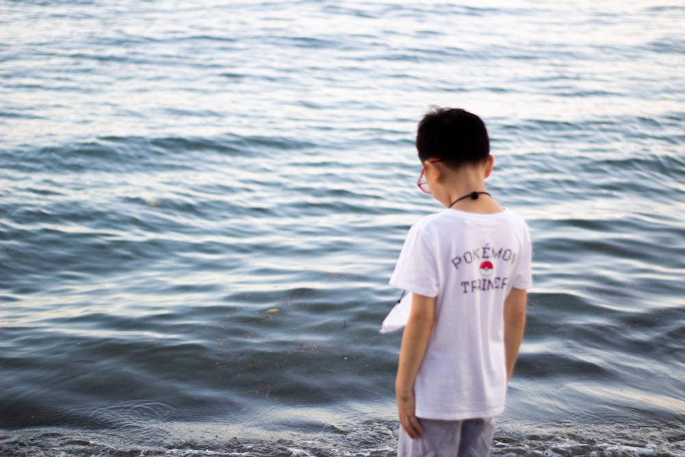 a young boy standing on a beach next to a body of water