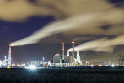 A panoramic view of a sprawling industrial power plant at dusk, illuminated with bright operational lights.