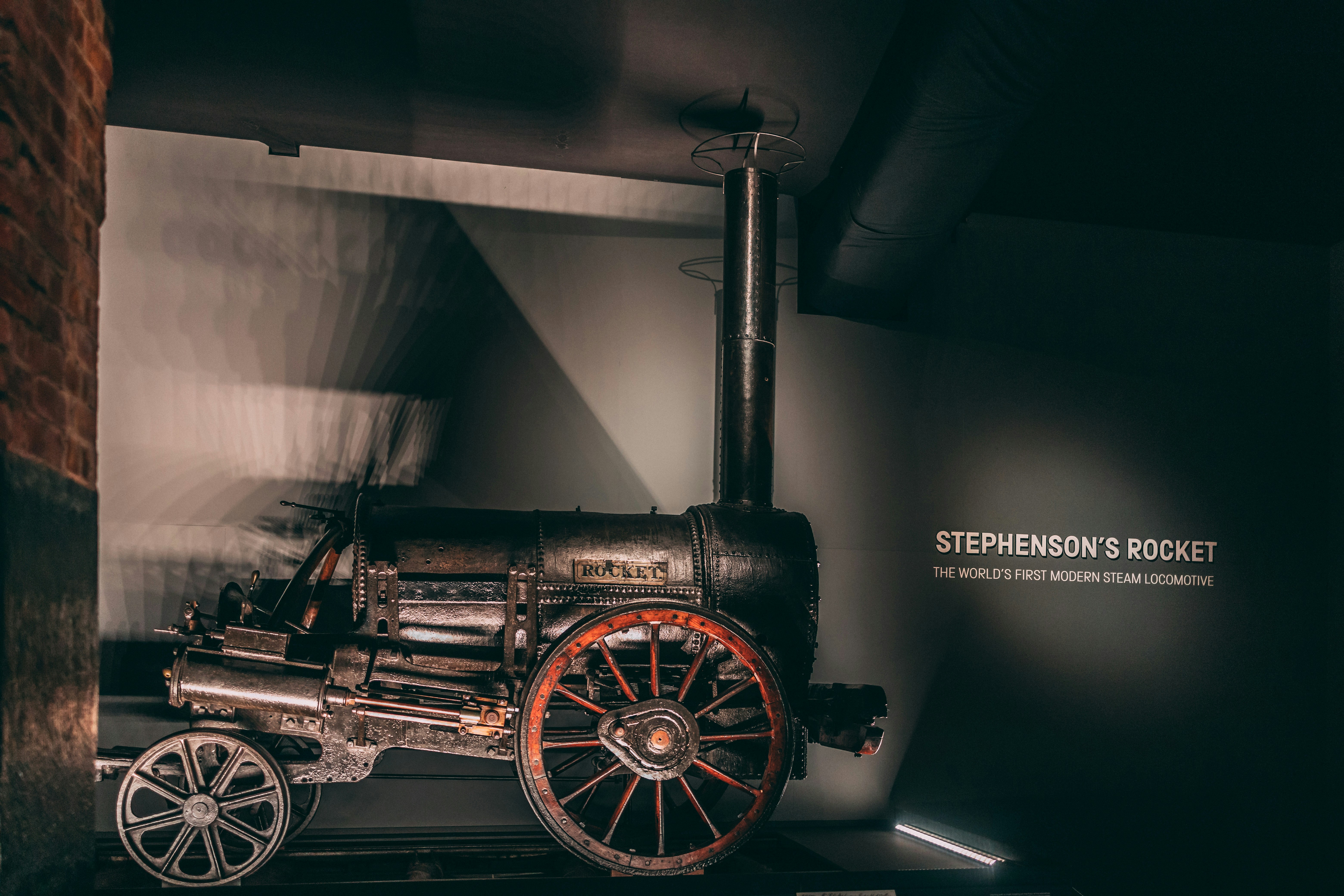Ornate Victorian steam locomotive with intricate brass arabesques and decorative marquetry paneling, dark museum setting, warm amber light