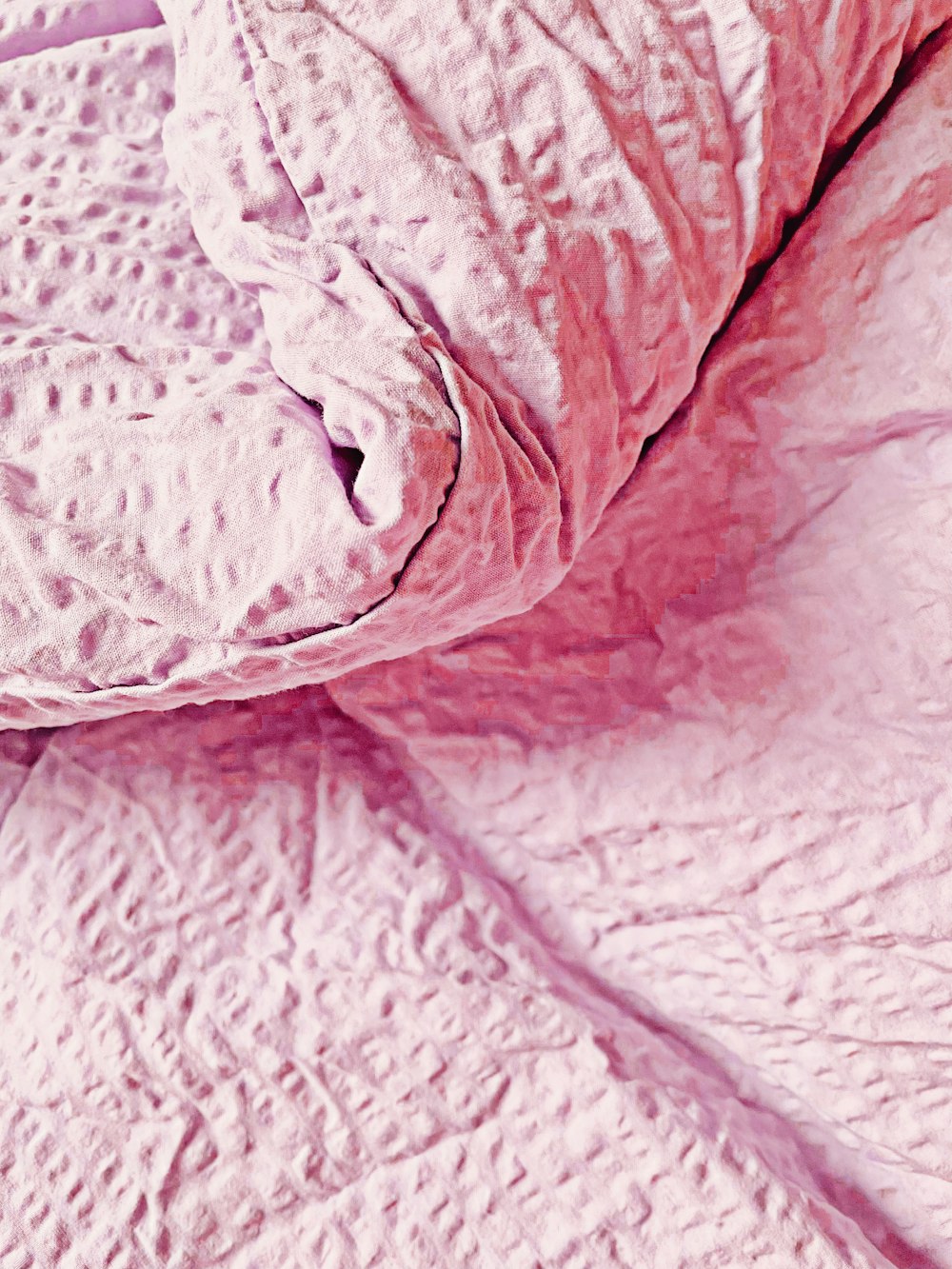 a close up of a bed with a pink comforter