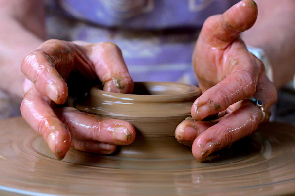 Clay art pieces in progress with fingers shaping soft, textured pottery on a wheel.
