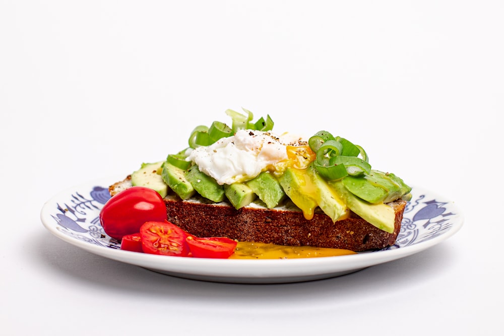 a white plate topped with a piece of bread covered in avocado