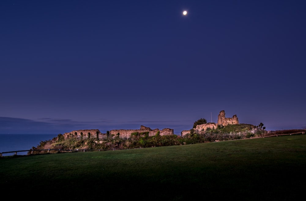 a castle on a hill at night with the moon in the sky