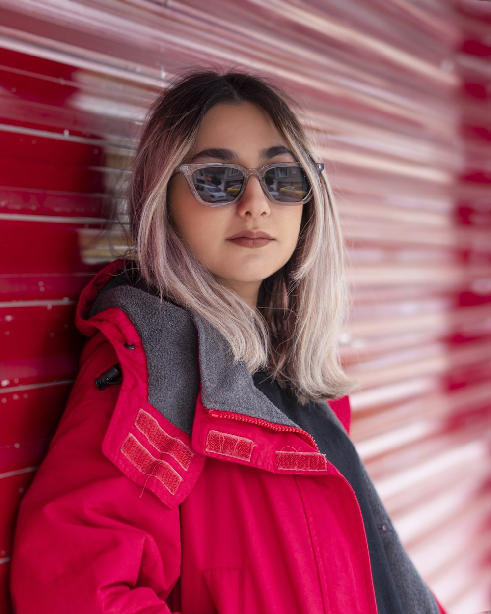 a woman in a red jacket leaning against a red wall