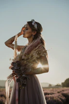 a woman standing in a field holding a bouquet of flowers