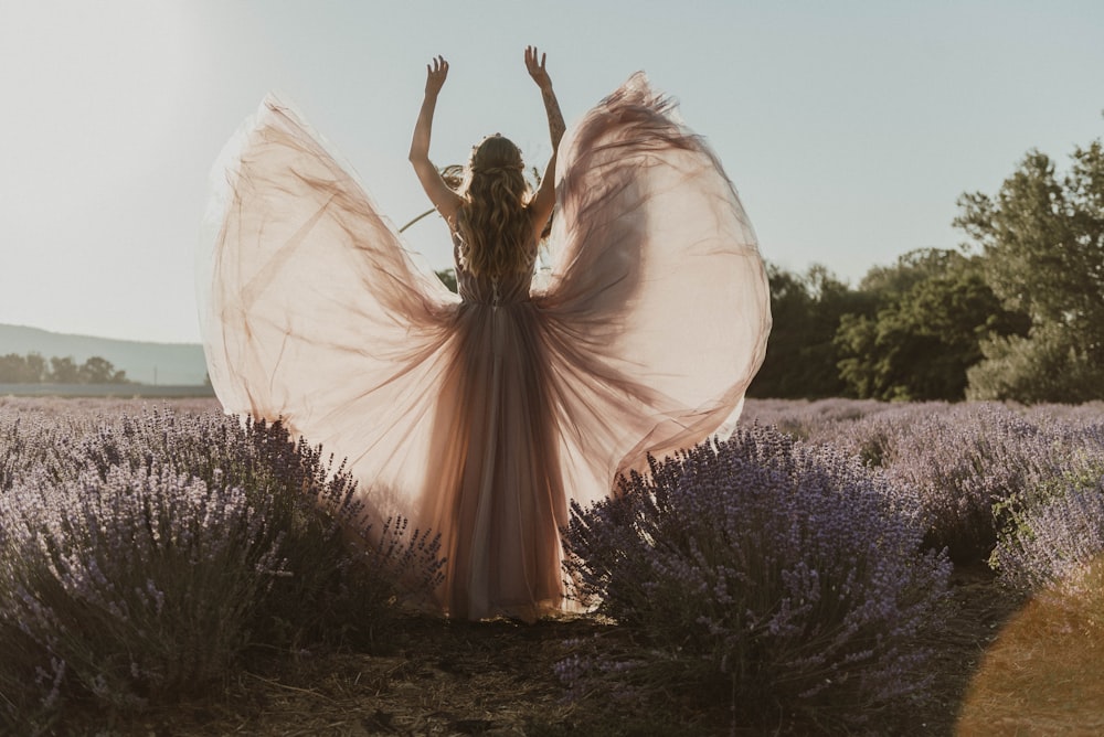 uma mulher de pé em um campo de lavanda com os braços no ar