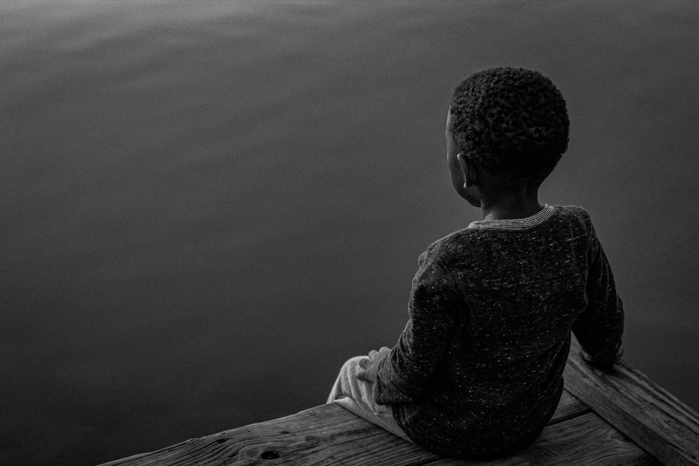 a young boy sitting on a dock looking at the water