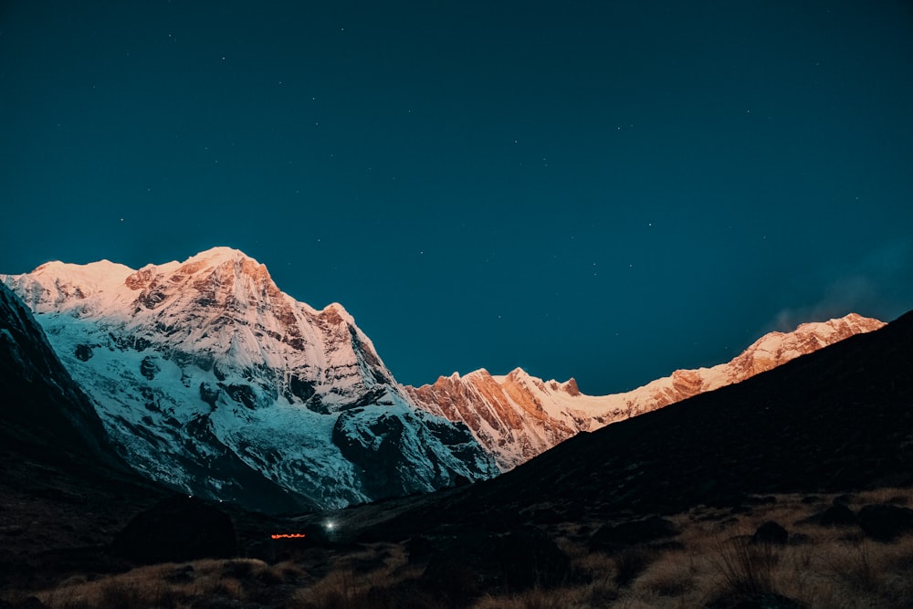 a snow covered mountain at night with the moon in the sky