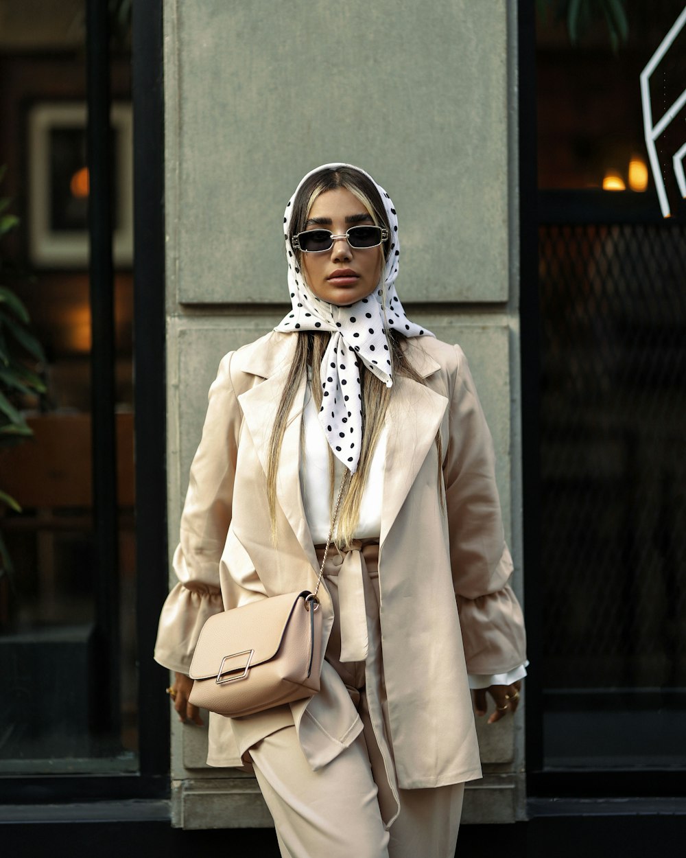 a woman in a beige suit and white polka dot scarf