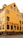 A yellow, multi-story building with large windows and the red lettering 'NYHAVN 17' on the facade. The street in front features people walking and small green plants in wooden barrels beside outdoor seating. The architecture suggests a historic or tourist area.