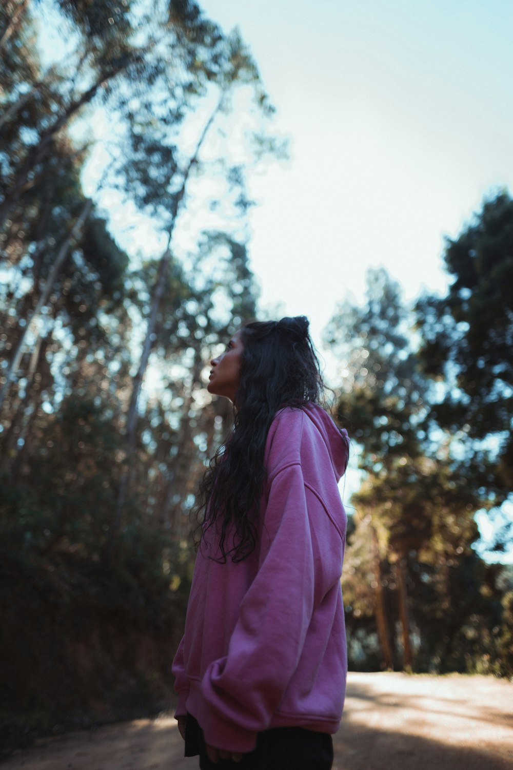 a woman in a pink hoodie standing on a dirt road