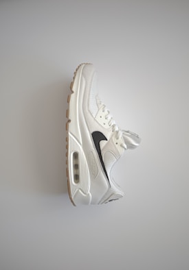 A single white athletic sneaker with a black swoosh design and gum-colored sole, positioned against a plain light background. The shoe features a visible air cushioning unit on the side and textured mesh surfaces.