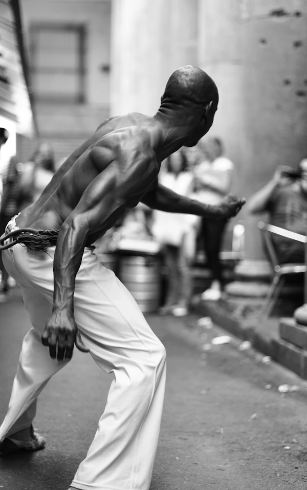 A capoeirista balanced on one leg with his arms raised