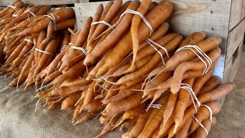 Fresh carrots neatly arranged in a rustic wooden crate on a sunny farm field.