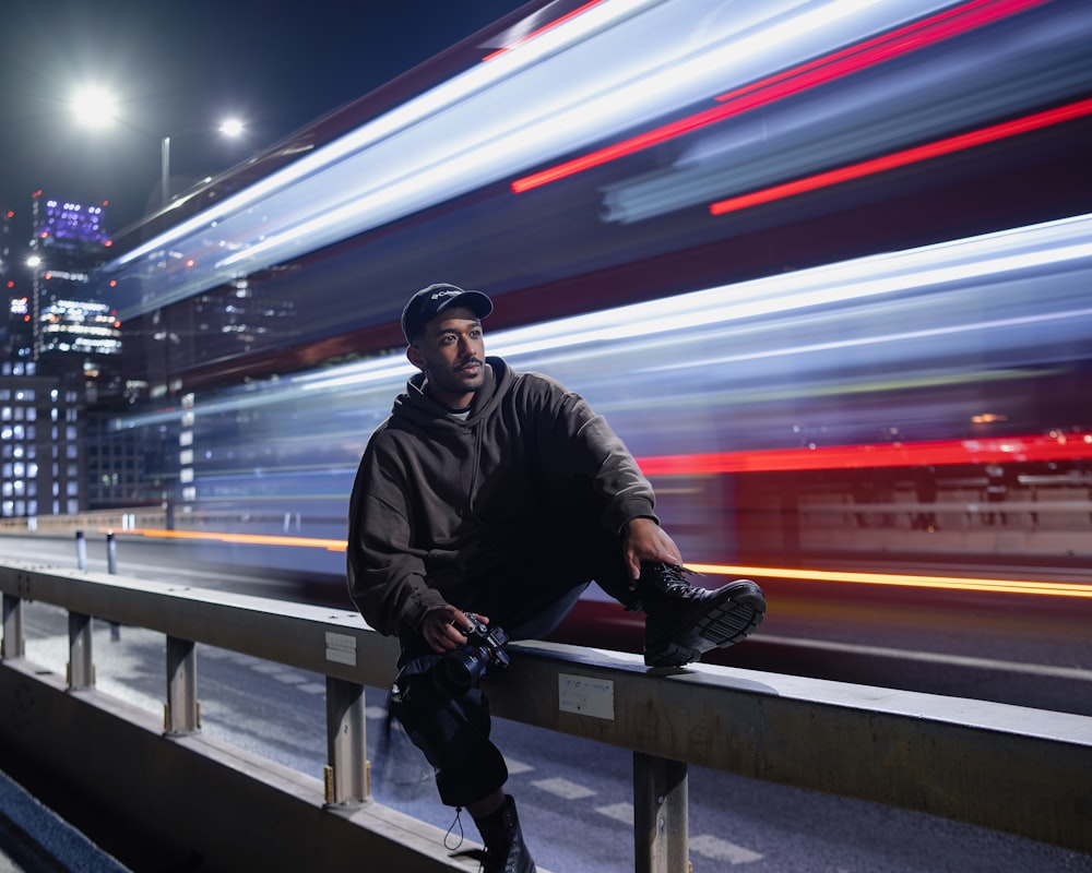 a man sitting on a rail next to a city street