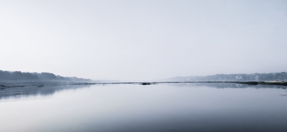 a body of water surrounded by trees and fog