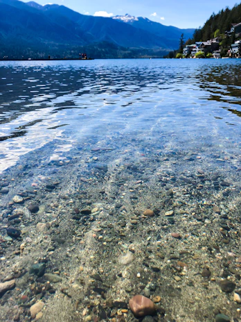 A geologist examining water samples by a serene mountain spring under clear skies.