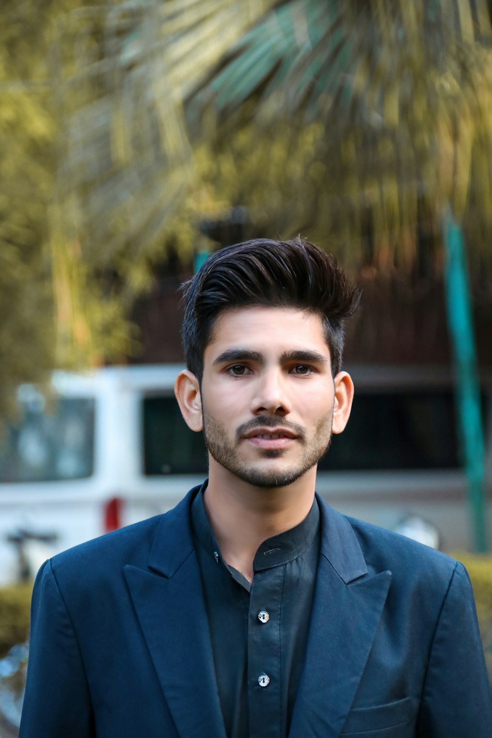 a man in a suit standing in front of a palm tree