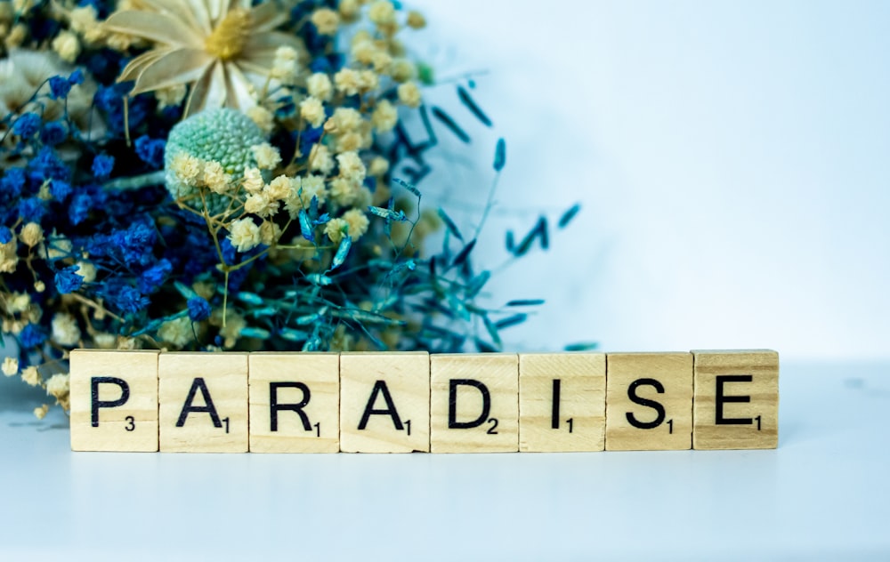 a wooden block spelling paradise next to a bouquet of flowers