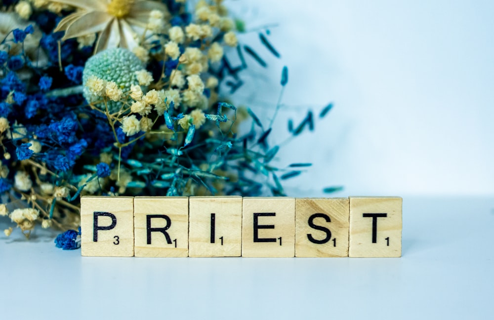 a wooden block spelling the word priest next to a bouquet of flowers
