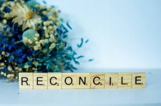 a scrabble block spelling the word reconcilie next to a bouquet