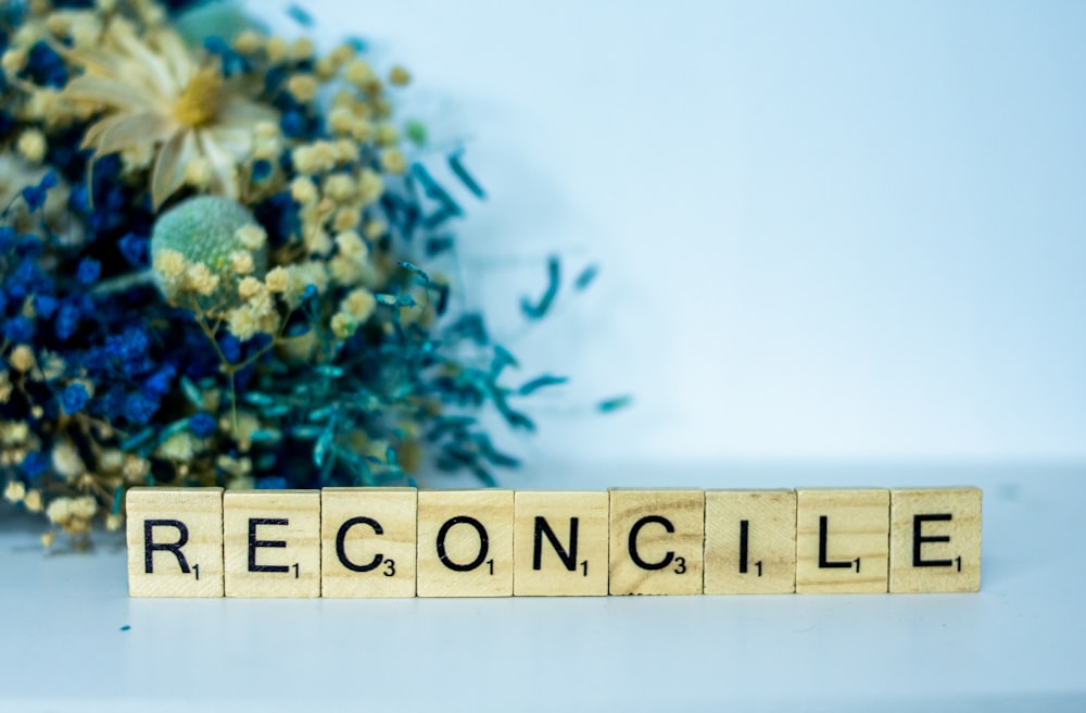 a scrabble block spelling the word reconcilie next to a bouquet
