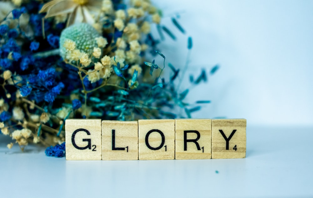 a wooden block spelling glory next to a bouquet of flowers