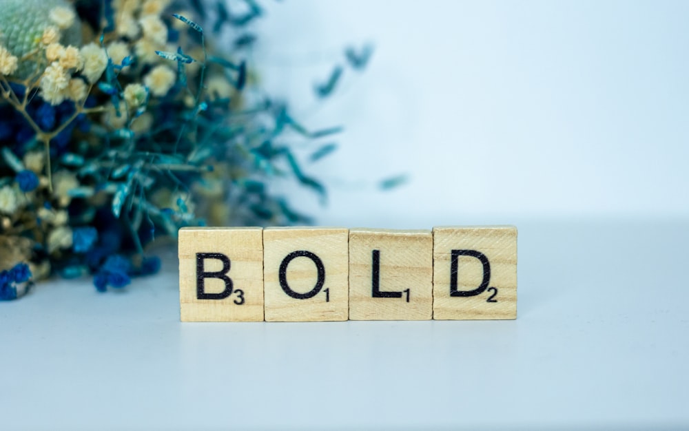 a wooden block that says bold next to a bouquet of flowers