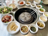 A table set with various Korean side dishes like kimchi, pickled radish, and fresh lettuce wraps.